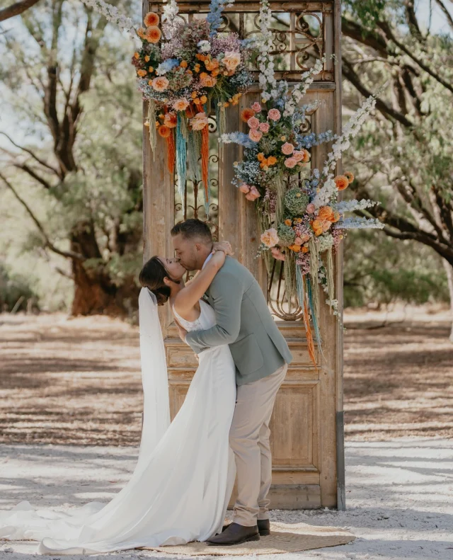 “MAKE sure you EAT on the wedding day.” – @daisymacc & @jay.bordas⁠
⁠
A love story that began with burpees (yes, really) and led to a dreamy, joy-filled celebration in the WA sunshine. ⁠
⁠
Daisy and Jay’s wedding at Solitaire Homestead was packed with meaningful moments – from surprise witnesses to custom florals and over 100 cardboard cutouts of their dogs!! ⁠
⁠
Tap through to Polka Dot Featured for more incredible details.⁠
⁠
Photographer: @placeoflove.photoandfilm / Cinematographer: @pineapplefingersau / Bride's Dress: @jrwbridal / Bridesmaid Dresses: @billy_j_boutique / Bride's Shoes: @novoshoes / Catering: @goannagourmetcatering / Ceremony Musicians: @adrianwilsonmusic / DJ: @adrianwilsonmusic / Engagement Ring: @gemstonewesternaustralia / Wedding Ring: @gemstonewesternaustralia / Flowers: @daisyandcloverflorals / Groom & Groomsmen Attire: @peterjacksonau / Makeup Artist: @soma._makeupartist / Sweet Treats: @harlequindessert / Signage: @lenedi.au / Venue: @solitaire_homestead / Transport: @Gannawayscharters⁠
⁠
[Image one description: Kissing in front of a giant wooden door standing in a forest clearing, this couple has just finished their ceremony. The groom is wearing a sage green jacket with tan pants, while the bride is dressed in a fitted white gown with an overskirt that flows behind her, accompanied by a pearl-encrusted veil. The door is decorated with stunning pink, blue and green florals.⁠
⁠
Image two description: The couple is now sitting at their ceremony, holding one finger of each other's hand as they drink their cocktails while guests mingle around them.]⁠
⁠
#PolkaDotWedding #FeelGoodWeddings #AustralianWeddings #AustralianWedding #WeddingStory #WeddingStories #BushWedding #WesternAustraliaWedding #WeddingMemories #WeddingInspiration #WeddingInspo #RealWedding